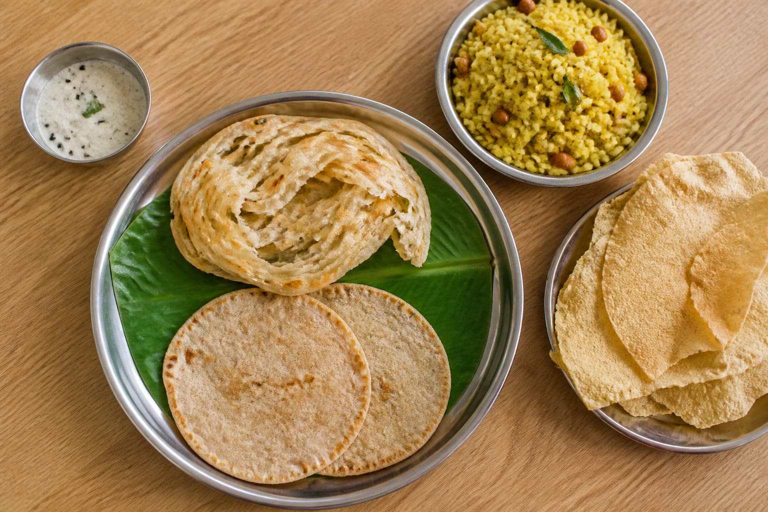 Beilagen von oben: aufgerissene Parotta, zwei Chapati, eine Schale Zitronenreis, Kokoschutney und ein Stapel Papads