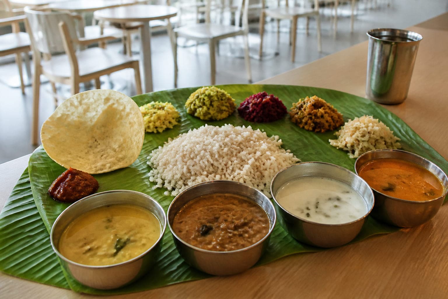 Kerala Meals auf Bananenblatt von schräg oben: Reis, fünf Gemüsebeilagen an der oberen Kante, Papad und Pickle