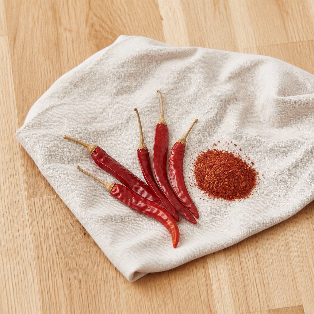 Fünf getrocknete rote Chilischoten neben grob gemahlenem Chilipulver